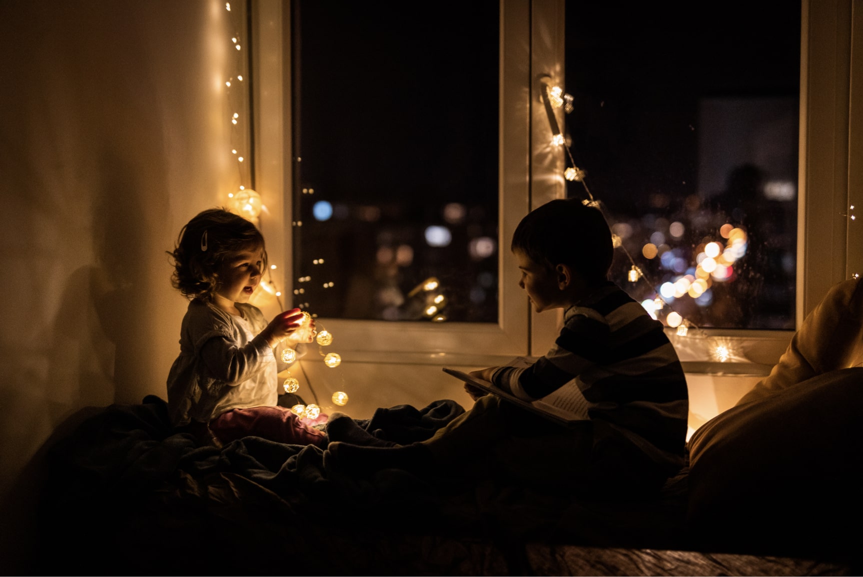 2 children playing under string lights in a darkend room